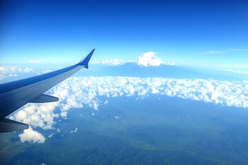 View from airplane window showing wing over clouds and distant land under a blue sky