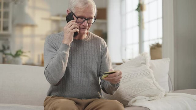 Mobile fraud, portrait of old man talking by phone with scammers, holding card. Elderly male person reporting data of his credit card by cellphone, data theft and stealing money from card, feed sad
