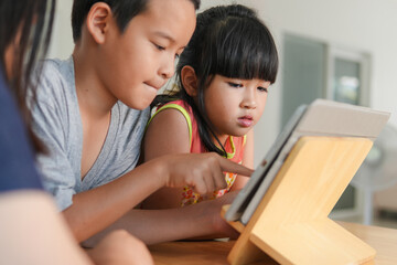 Obraz premium A cute asian young girl and her brother use tablet for education or social media in the home,Concept of people using technology, Communication and social media in daily life,candid and ordinary style.