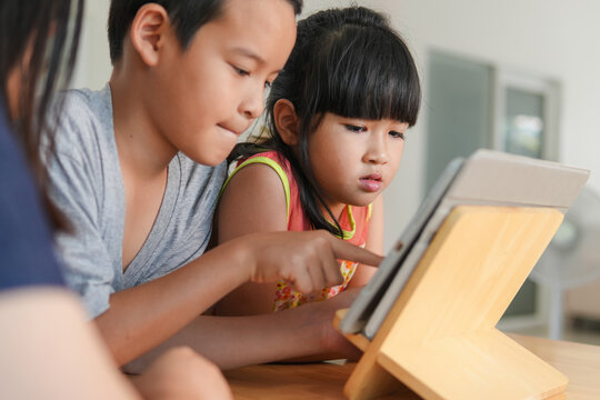 A cute asian young girl and her brother use tablet for education or social media in the home,Concept of people using technology, Communication and social media in daily life,candid and ordinary style.