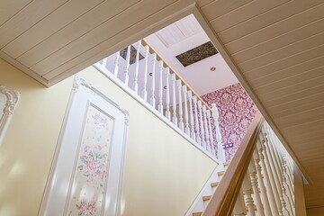 Low-angle shot of interior stairs with white railings, pale yellow walls, and a patterned floral...