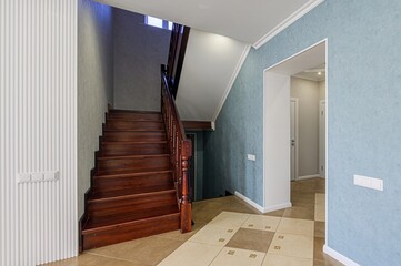 interior shot showcasing a staircase with wooden steps and a hallway with tiled floors. The walls...