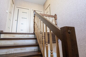 Interior shot of a staircase with wooden steps and railing, leading to a hallway with doors....