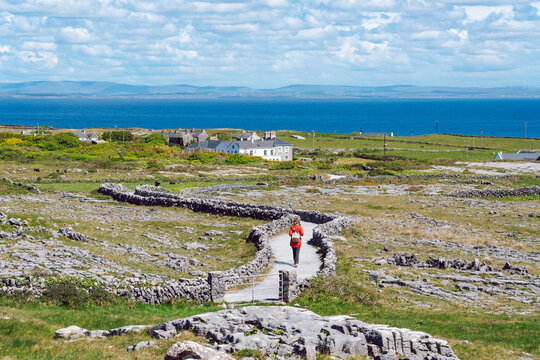A tourist walking a trail on Inishmore on Aran Islands with endless stone walls and the vast Atlantic stretching to the horizon.