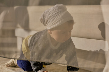 Little baby girl is playing behind the white curtains outdoors.