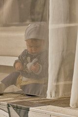 Little baby girl is playing behind the white curtains outdoors.