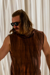Portrait of a long haired bearded man in a brown t-shirt and sunglasses chilling in the hotel.