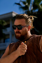 Portrait of a long haired bearded man in a brown t-shirt and sunglasses chilling in the hotel.