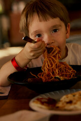 Little boy eating a spaghetti with tomato sauce.
