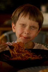 Little boy eating a spaghetti with tomato sauce.