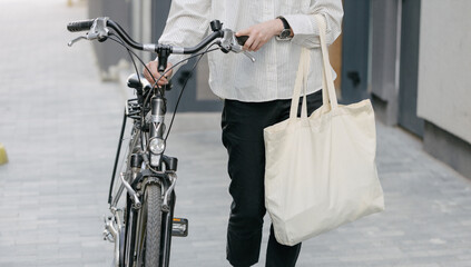 Obraz premium Woman holding eco bag or cotton tote bag in the city while riding a bike