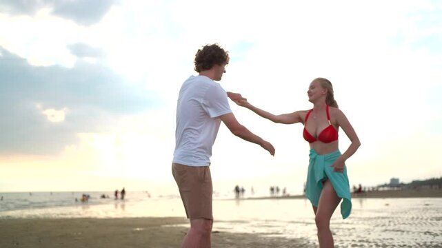 Romantic white Western couple walking and playfully teasing each other along the beach at sunset.