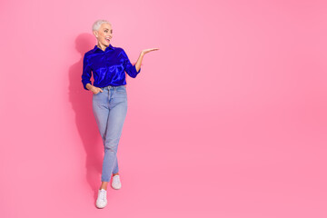 Smiling mature woman in casual and stylish attire posing against a vibrant pink background,...