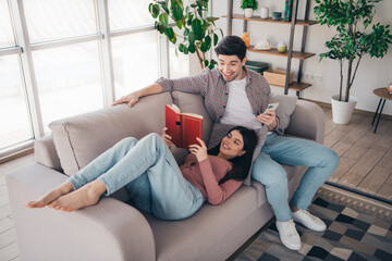 Obraz premium Young couple enjoying leisure time together reading and smiling in a cozy living room setting during a relaxed day indoors.