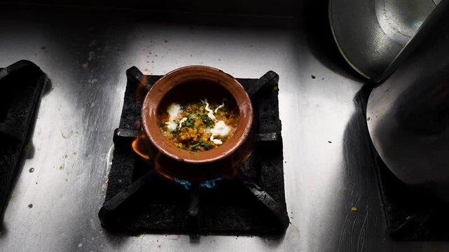 Chicken handi with cream and herbs simmers in clay pot over flame at Pakistani restaurant. Lahore, Pakistan