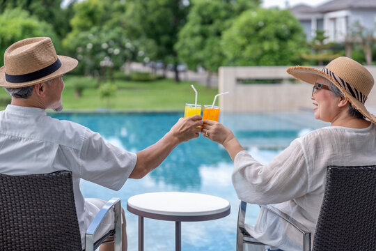 happy senior couple enjoy talking with freshy drink on table,sitting,relaxing by the pool,elderly people travel destination tropical resort and spa on summertime