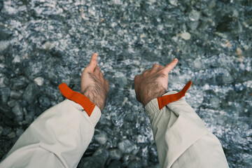A person in a light jacket crouches by a cold, rocky stream in Mount Olympus, dipping hands near the flowing water.
