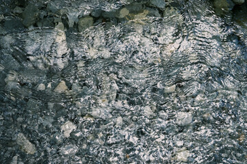 Rippling surface of a crystal-clear mountain stream in Mount Olympus, revealing smooth pebbles and rocks beneath the water.
