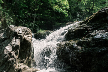 Refreshing waterfall splashes over rugged mossy rocks in the forest of Mount Olympus, creating a vibrant and natural scene.
