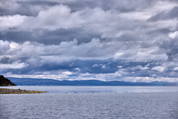 A scenic view of Lake Titicaca’s northern side from the Capachica Peninsula, showing Andean hills, deep blue waters, and traditional farmland under dramatic stormy skies.