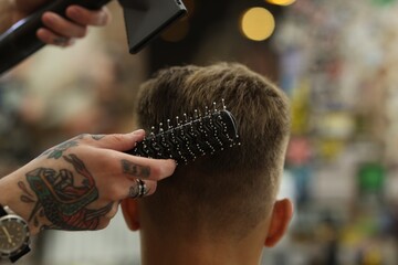 Professional barber blow drying client's hair in barbershop, closeup