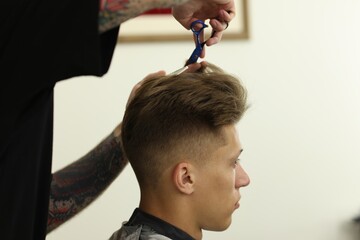 Professional barber cutting client's hair with scissors in barbershop, closeup