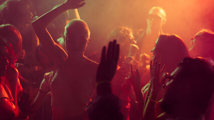 Vibrant party scene with diverse individuals dancing in a dimly lit, smoke-filled club with vibrant red and orange lighting. Concept of party, youth, nightclub, celebration