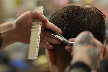 Professional barber cutting client's hair with scissors in barbershop, closeup