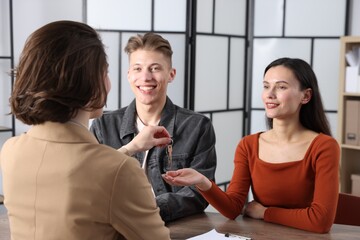 Real estate agent giving house key to new owners at table indoors