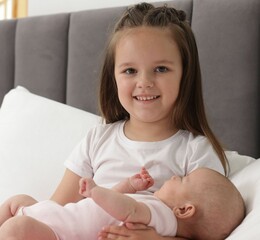 Cute girl and her little sister on bed at home