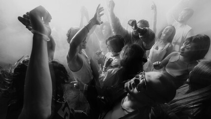 Black and white photo of a lively crowd dancing with hands raised, creating an energetic atmosphere. Concept of party, youth, nightclub, celebration.