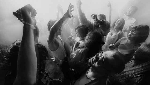 Fototapeta Black and white photo of a lively crowd dancing with hands raised, creating an energetic atmosphere. Concept of party, youth, nightclub, celebration.