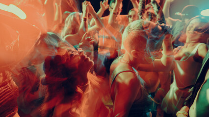 Blurred image of dancing crowd at a vibrant, colorful nightclub party, in a dimly lit, smoke-filled...