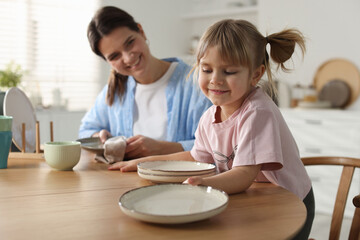 Little girl helping her mom wiping plates at table in kitchen