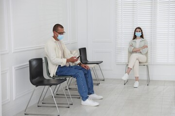 Man and woman in medical masks waiting for appointment indoors