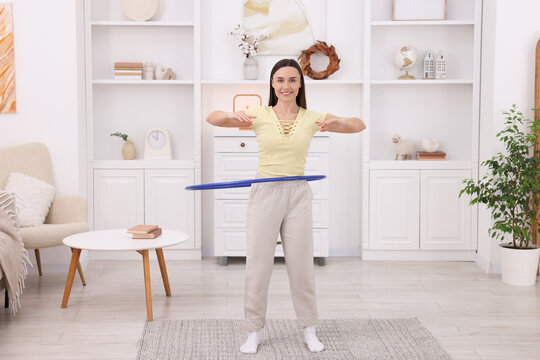 Smiling woman training with hula hoop at home