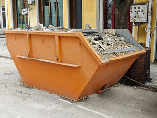 Orange Industrial Dumpster Full of Construction Debris and Rubble on Urban Street. Building Renovation Waste Management and Cleanup Concept
