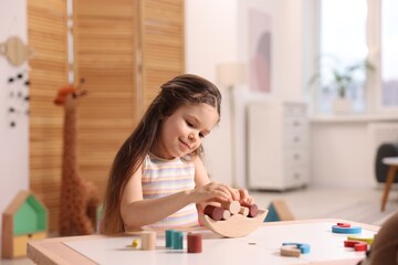 Motor skills development. Little girl playing with wooden balance toy at table indoors