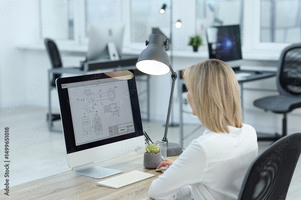 Poster technician making digital engineering drawing on computer at desk in office, back view