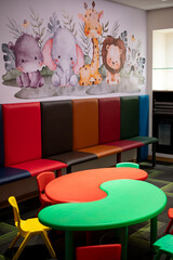 Colorful plastic chairs and tables for kids in play area with cartoon elephant and giraffe wall...