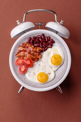 Breakfast of fried eggs with bacon or sausage and vegetables. ? plate on a vintage alarm clock