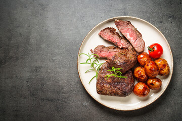 Meat steaks with vegetables and herbs at black board.