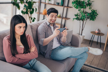 Obraz premium Young couple sitting together on a couch in a stylish living room, showcasing contrasting emotions and reactions