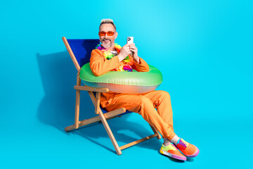 Stylish mature man in orange outfit relaxing with inflatable pool toy in vibrant blue studio setting