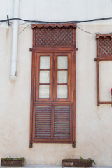 Traditional wooden window in Bushehr, Iran, showcasing intricate latticework and shutters, set against a weathered wall with potted plants below.