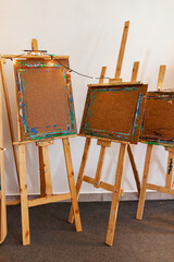 Horizontal view of art easels with heavy use, framed by string lights. One panel features sketch of...