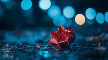 A single red paper flower on the ground with bokeh lights in the background