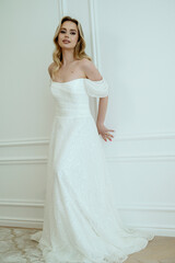 Fototapeta premium Blonde bride standing in light interior in long wedding dress