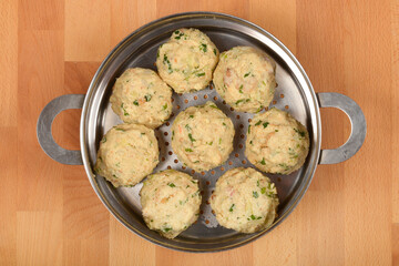 Bread dumplings with specks of herbs, placed in a metal steaming pot on a wooden surface ready for cooking