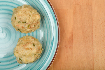 Overhead shot shows two cooked bread dumplings with specks of green herbs, placed on a blue ceramic plate with a wooden background